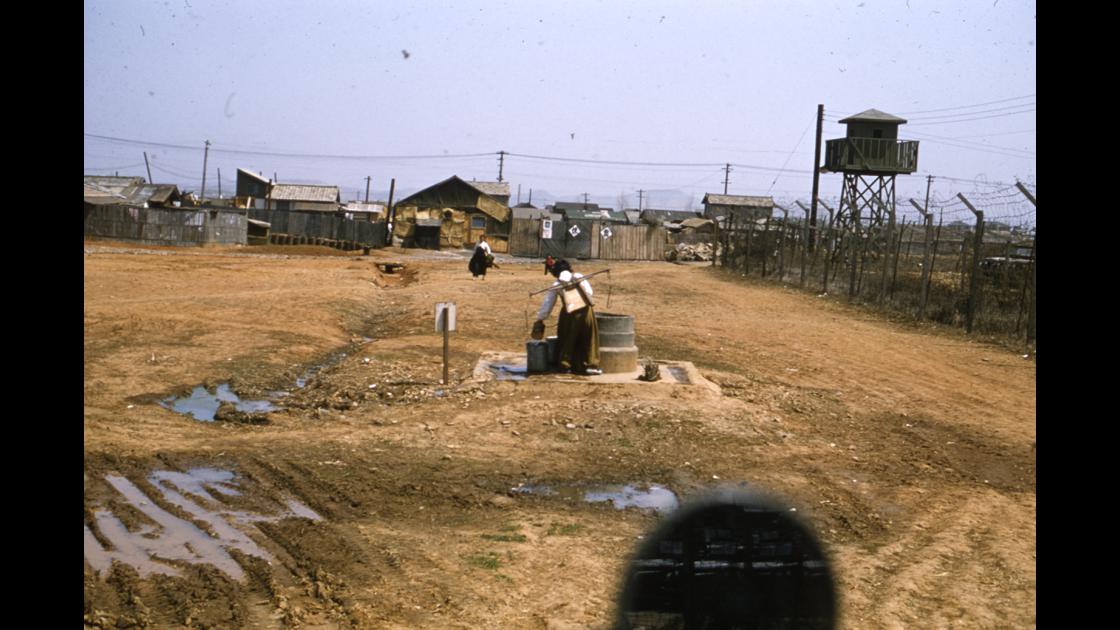 1953년 대구 K-2비행장 외곽 철조망 옆 마을 우물에서 물을 긷고있는 여인과 연탄공장 썸네일