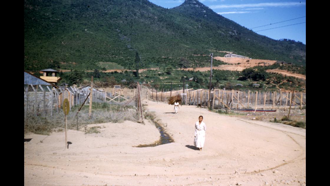 1952년 거제도의 포로수용소 철조망이 둘러싼 사이 길을 걸어오는 할머니와 나뭇꾼 썸네일