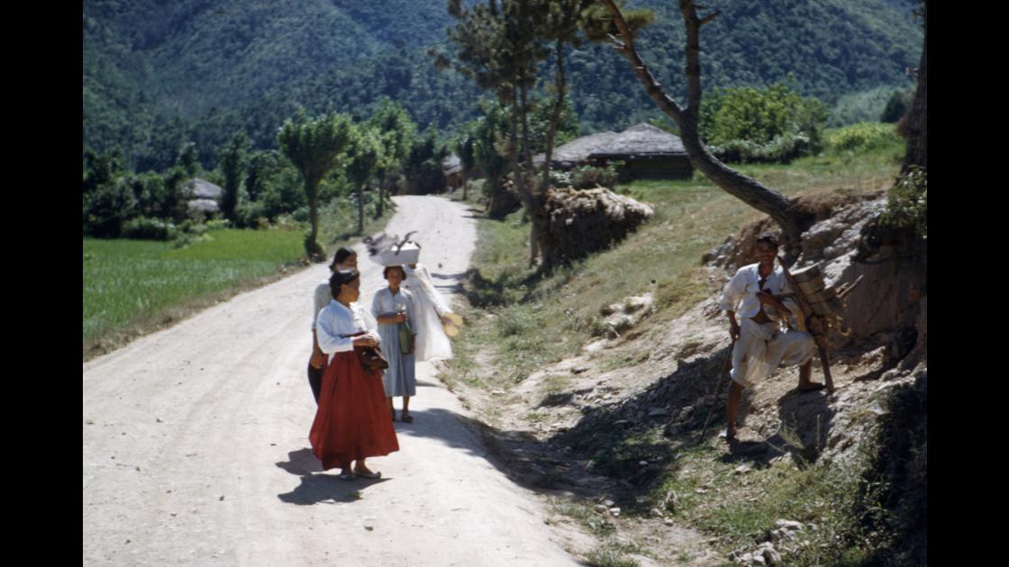 1953년 거제의 도로 옆에 쉬고있는 나무를 진 지겟꾼과 서로 이야기하는 여인들 썸네일