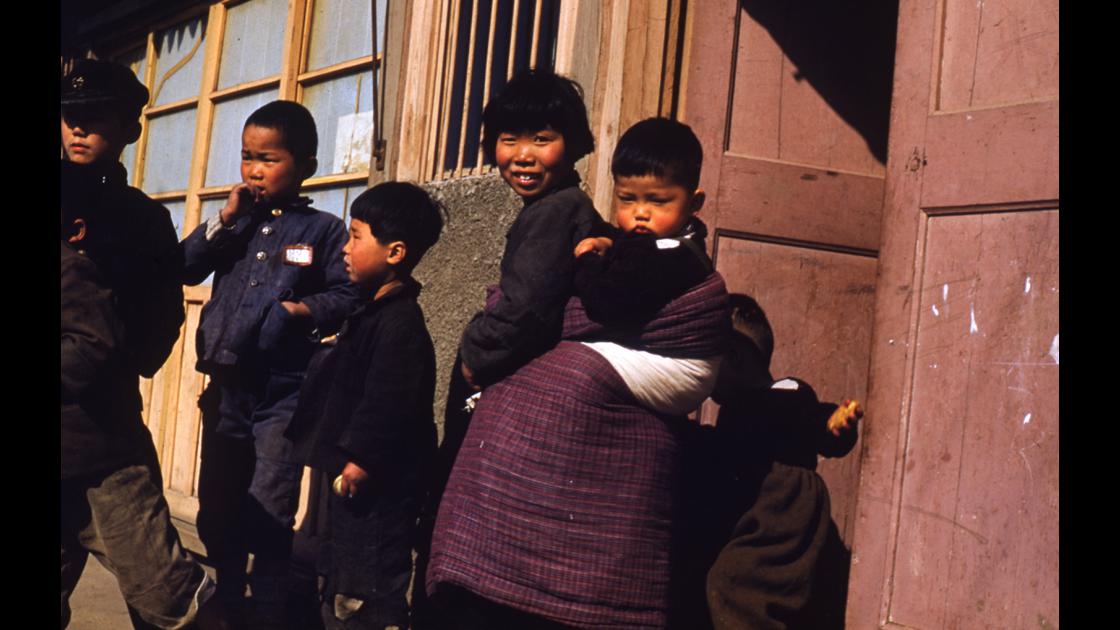 1952년 경남 진해 도로변 집 대문 앞에서 동생을 업고 돌보는 여자 아이와 동네 꼬마들 썸네일